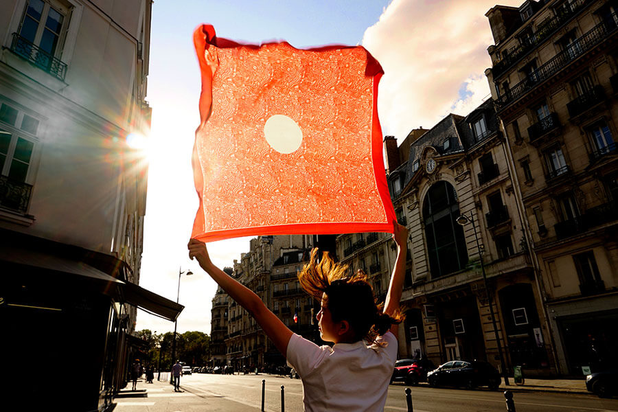 woman holding red scarf with circle against sun