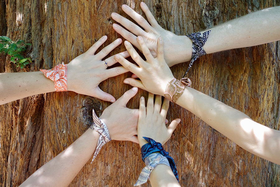 five hands with colorful printed silk wristbands on a tree