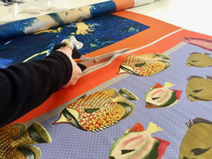 a person hand cutting printed silk panels on the table