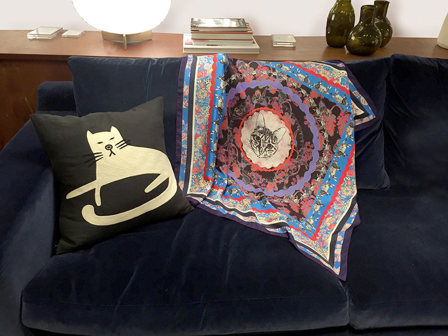 foulard en soie coloré avec un motif de chat au centre, à côté d'un coussin sur un sofa