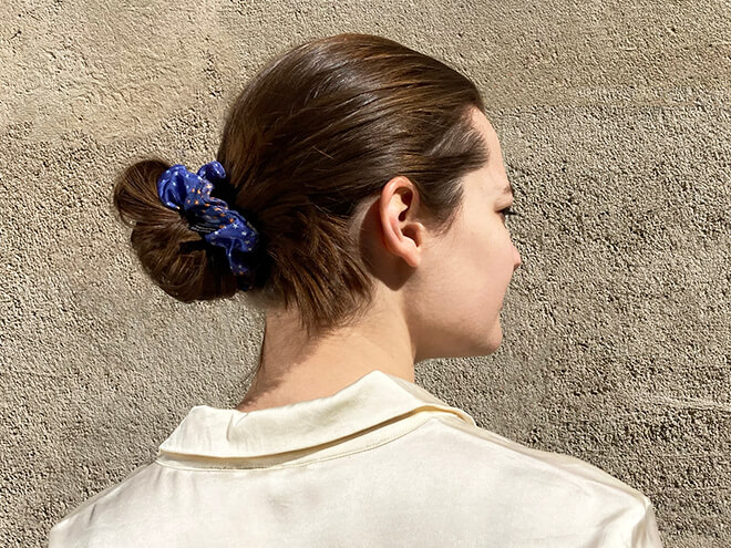 jeune fille parisienne portant une chemise blanche et un chouchou en soie bleu dans ses cheveux
