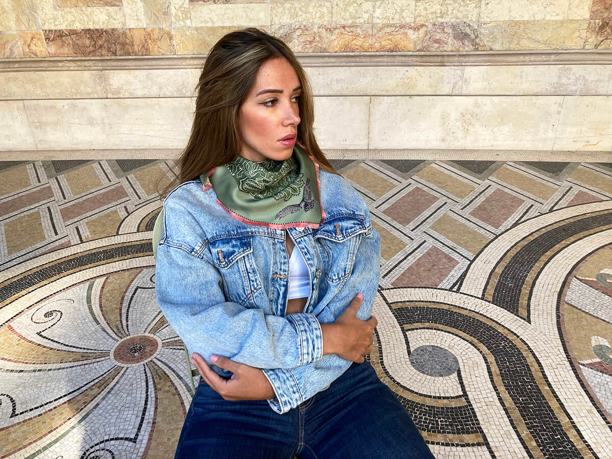 young lady wearing jean and a green silk scarf with marble wall in the background
