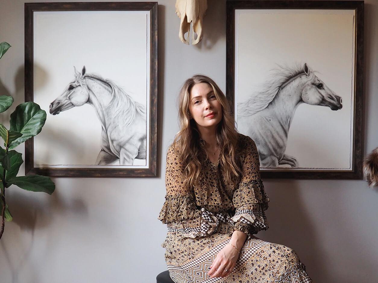 blond artist with horse drawings hanged on the wall in the background