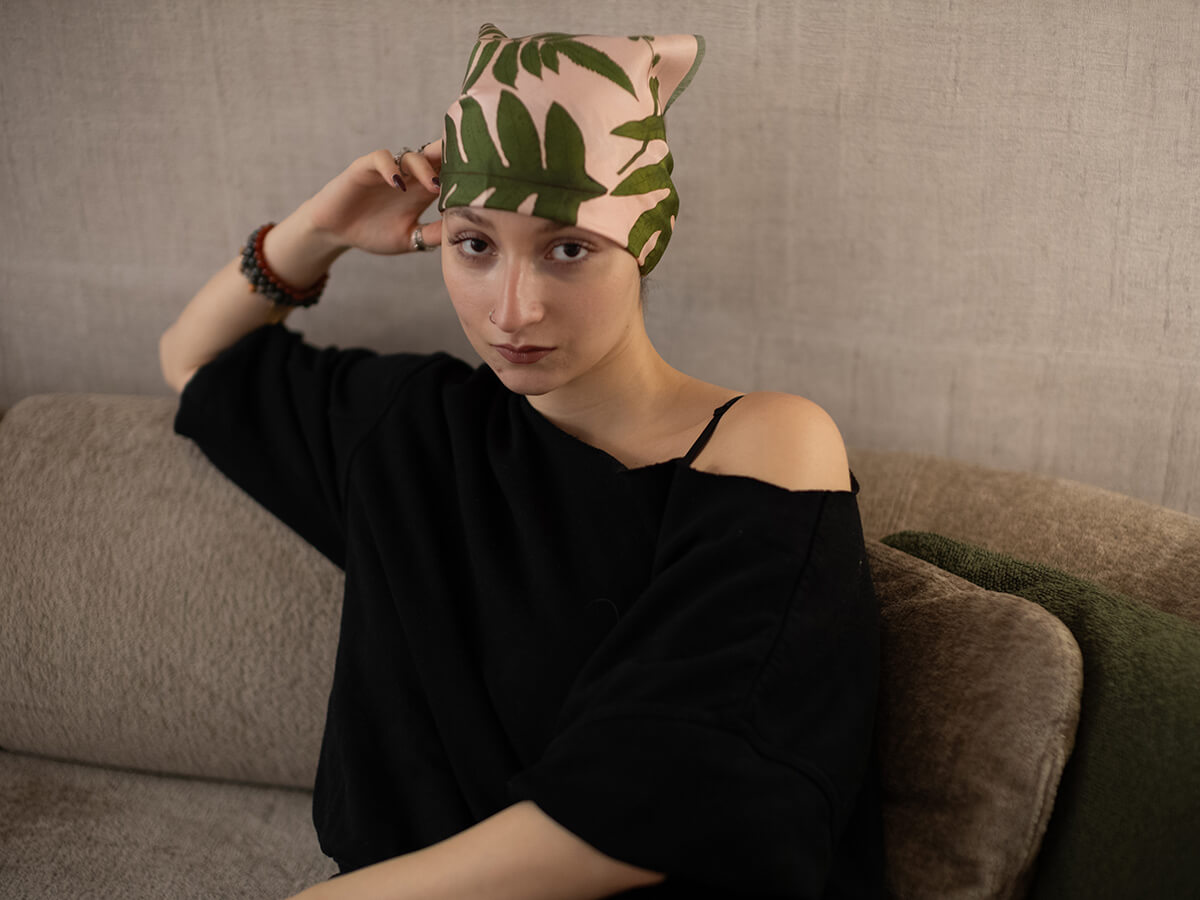 white woman wearing a black pull over and a pink silk scarf with leaves motif tied around her head