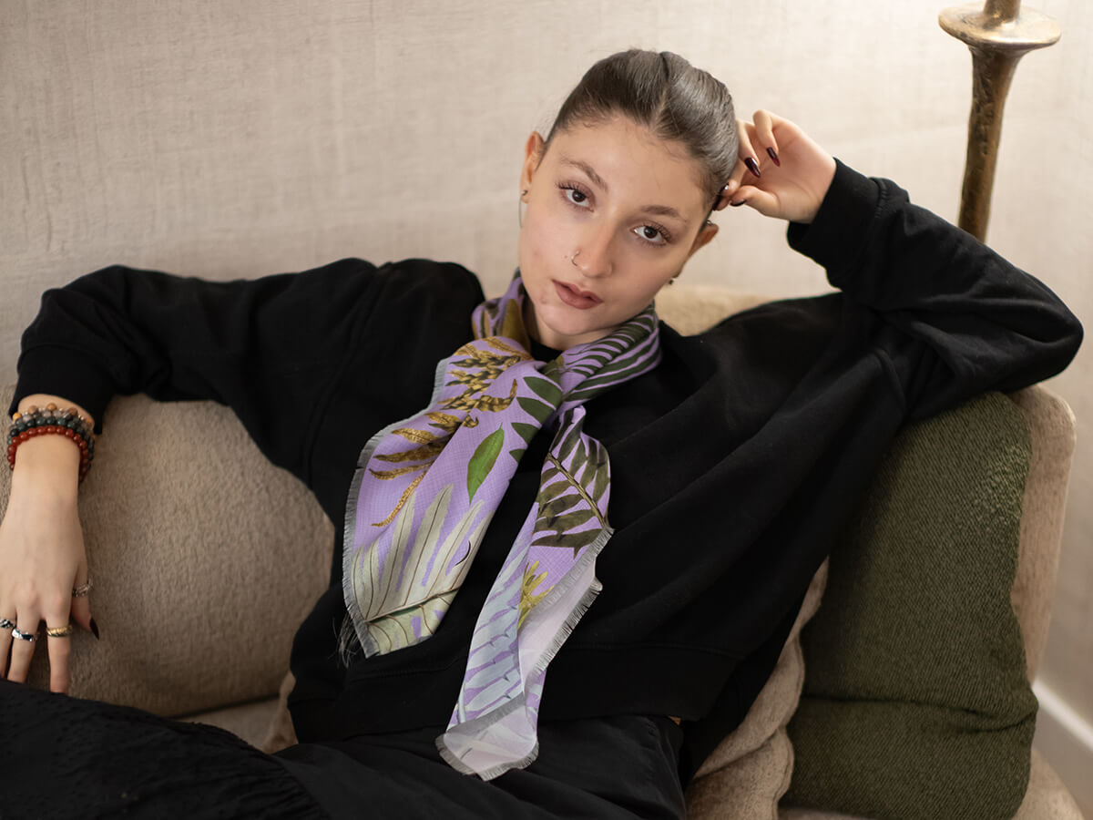 white woman wearing a black pull over and a purple silk scarf with leaves motif tied around her neck