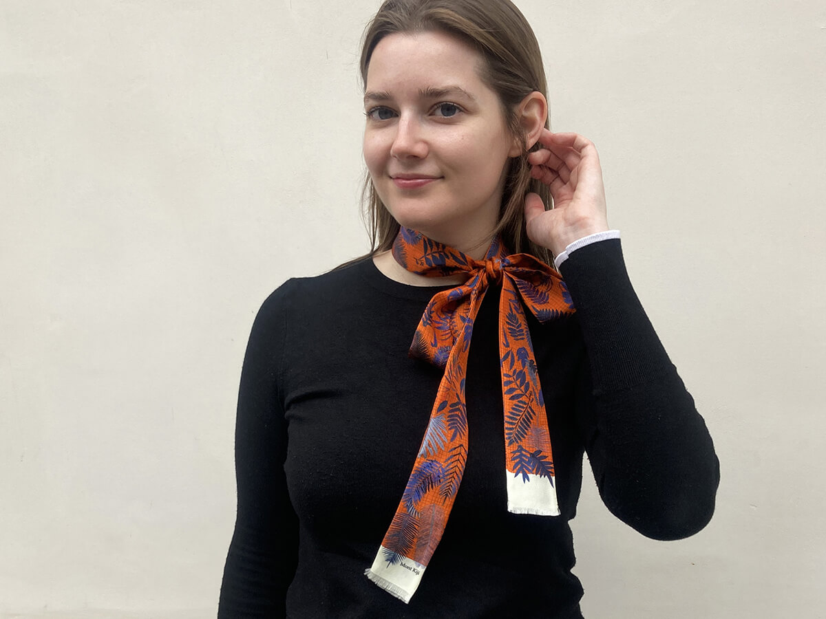 white woman wearing a black pull over and a red long silk scarf with leaves motif tied around her neck