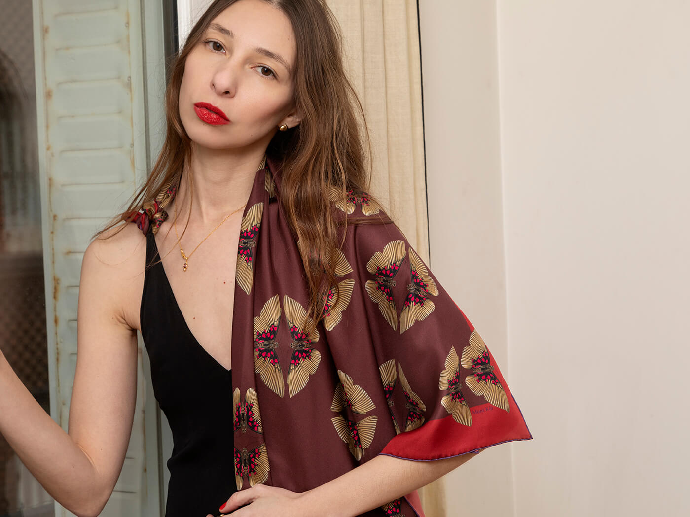 white woman wearing a red silk scarf with butterfly motif with a black jacket