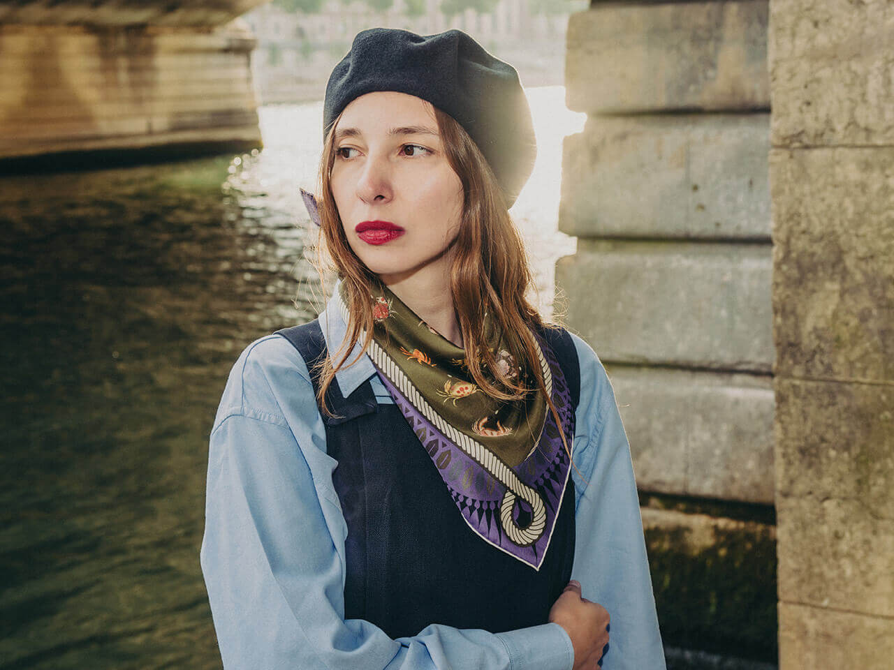 white woman wearing a dark silk scarf with crab motif around her head with a blue shirt with river behind her